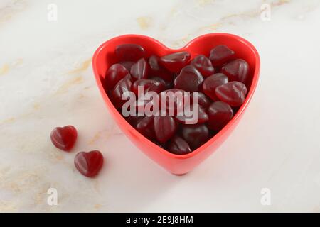 Red cherry heart gummy candies on red Valentine`s Day heart shaped bowl on table Stock Photo